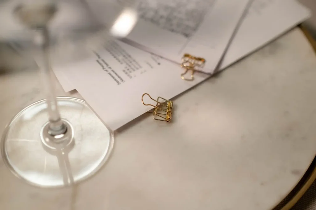 Close-up of documents and paperclips on a table with a wine glass, showcasing a refined workspace.
